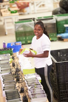 A black woman smiles at the camera, while holding the package for an assembly she is kitting at RiverSide Integrated Solutions.