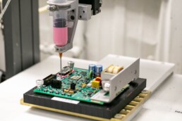 A cobot at RIS automatically dispenses adhesive in a precise area on a circuit board.
